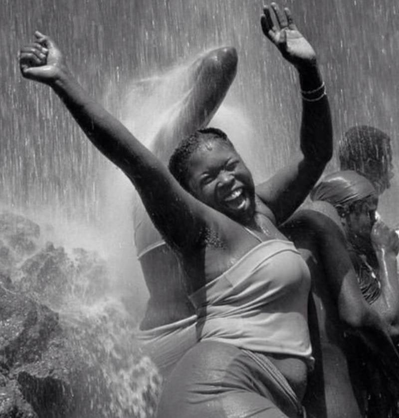 A woman in a rainstorm of spray, laughing with her arms raised, in black and white